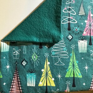 Puede incluir: Tela turquesa con un patr&oacute;n de &aacute;rboles de Navidad estilizados, estrellas y regalos. La tela tiene un respaldo de franela verde.