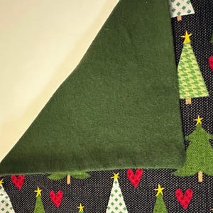May include: A close-up of a green fabric with a black fabric underneath. The black fabric has a pattern of green Christmas trees and red hearts.