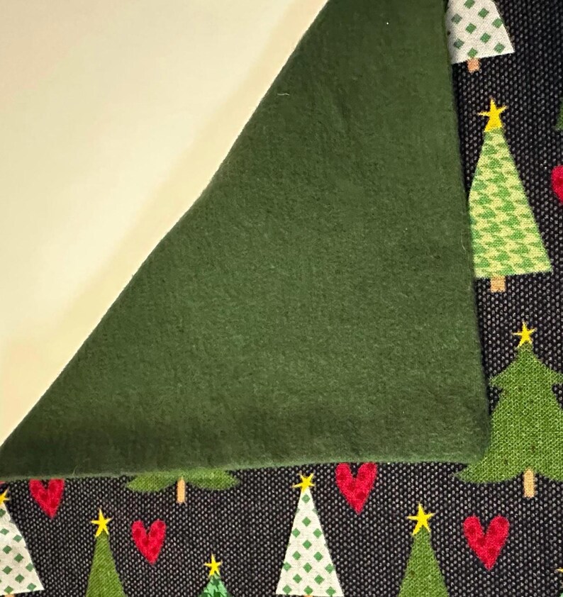 May include: A close-up of a green fabric with a black fabric underneath. The black fabric has a pattern of green Christmas trees and red hearts.