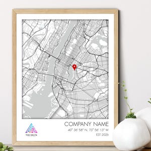 May include: Framed black and white map print of a city, with a red location marker. The print includes the company name, coordinates, and the year 2026. The Delta logo is in the lower left corner. The frame is a light wood color.