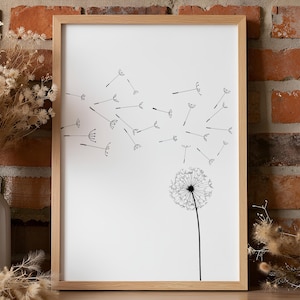May include: A framed wall art print featuring a black line drawing of a dandelion on a white background. The dandelion head is at the bottom right, with its seeds blowing upward and across the frame toward the left in a scattered pattern.