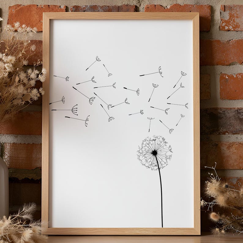 May include: A framed wall art print featuring a black line drawing of a dandelion on a white background. The dandelion head is at the bottom right, with its seeds blowing upward and across the frame toward the left in a scattered pattern.