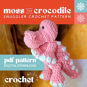 Puede incluir: Un juguete de cocodrilo rosa tejido a ganchillo con manchas blancas, titulado "Moss the Crocodile Snuggler Crochet Pattern". La imagen también incluye el texto "PDF Pattern Digital Download" y "Crochet by Cate".