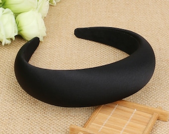May include: A black padded headband for hair. The headband is thick and wide, and has a smooth, matte finish.