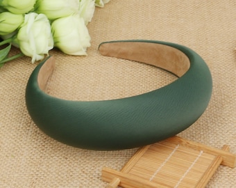 May include: A dark green padded headband for hair. The headband is made of a soft, smooth material and is designed to be comfortable to wear.
