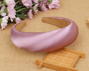 May include: A wide, padded headband made of soft, light purple satin. The headband is curved and has a smooth, polished finish.