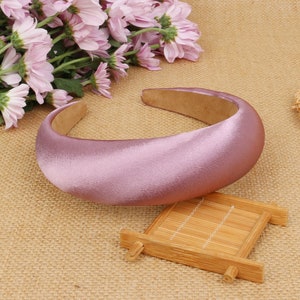 May include: A wide, padded headband made of soft, light purple satin. The headband is curved and has a smooth, polished finish.