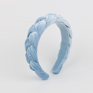 Puede incluir: Una diadema de terciopelo azul claro con un diseño trenzado. La diadema está hecha de un material suave y cómodo y es perfecta para agregar un toque de elegancia a cualquier atuendo.