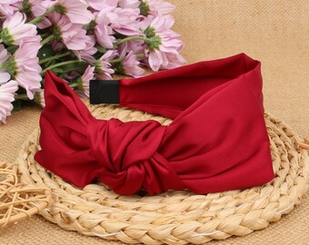May include: A red satin headband with a large knotted bow. The headband is on a woven surface.