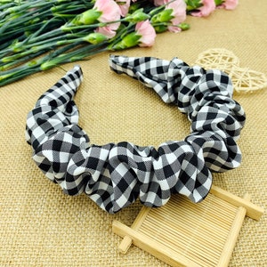 May include: A black and white gingham patterned headband. The fabric is gathered and ruched, creating a textured appearance. The headband is a classic accessory, suitable for various hairstyles and occasions.