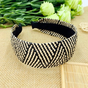 May include: Black and beige woven headband with a geometric pattern. The headband is made from a natural material and has a black elastic band.