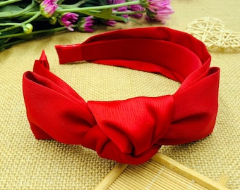 May include: A red fabric headband with a large knotted bow. The headband is made of a soft, stretchy material and is perfect for adding a touch of style to any outfit.
