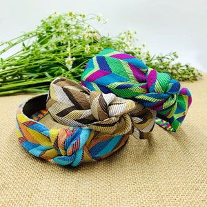 May include: Three colourful patterned headbands with knotted bows. The headbands are made of fabric with a geometric design in shades of blue, green, yellow, brown, and pink.