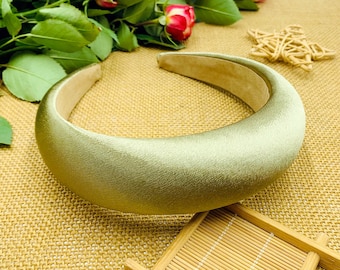 May include: A sage green satin headband. The headband is thick and wide, and it is lying on a woven brown surface.
