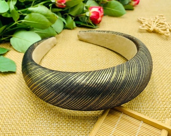May include: A wide black headband with a gold metallic finish. The headband has a textured, wavy pattern.