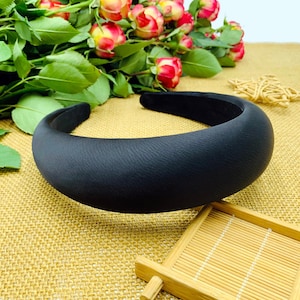 K&ouml;nnte beinhalten: Ein schwarzes gepolstertes Haarband. Das Haarband ist dick und breit und hat eine glatte, matte Oberfl&auml;che.