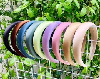 May include: A set of ten satin headbands in various colors, including black, brown, blue, green, purple, pink, and beige. The headbands are displayed on a white wire rack.