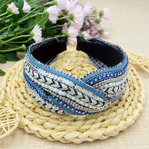 May include: A blue and white headband with a braided design and beaded embellishments. The headband is made of fabric and has a stretchy elastic band.