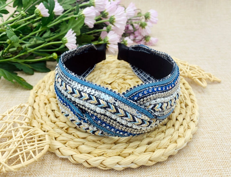 May include: A blue and white headband with a braided design and beaded embellishments. The headband is made of fabric and has a stretchy elastic band.