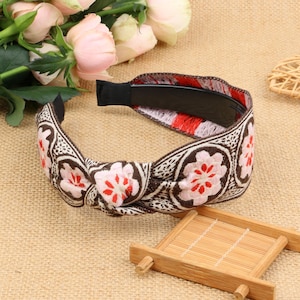 May include: A brown and white headband with a floral pattern and a red accent. The headband is tied in a knot at the top.