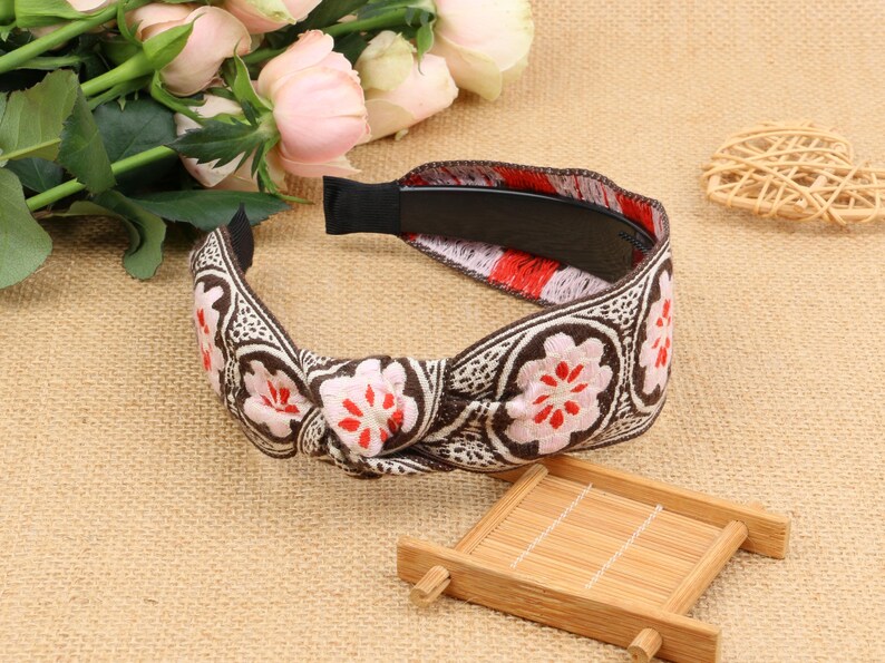 May include: A brown and white headband with a floral pattern and a red accent. The headband is tied in a knot at the top.