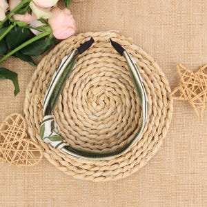 May include: A green and white patterned headband with a knot on the side. The headband is lying on a woven straw surface.