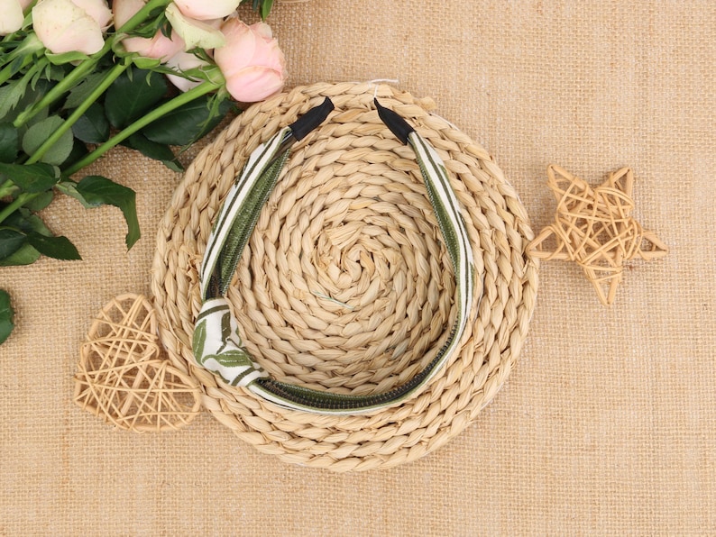 May include: A green and white patterned headband with a knot on the side. The headband is lying on a woven straw surface.