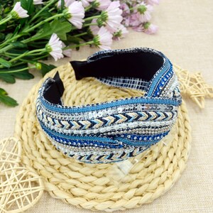 May include: A blue and white beaded headband with a knotted design. The headband is made of fabric and has a black elastic band.