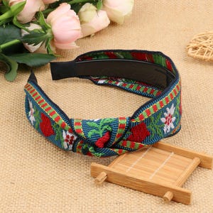 May include: A blue, green, red, and white headband with a floral pattern and a knotted design. The headband is made of fabric and has a black elastic band.