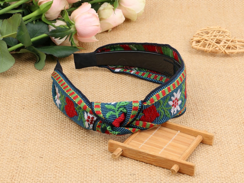 May include: A blue, green, red, and white headband with a floral pattern and a knotted design. The headband is made of fabric and has a black elastic band.