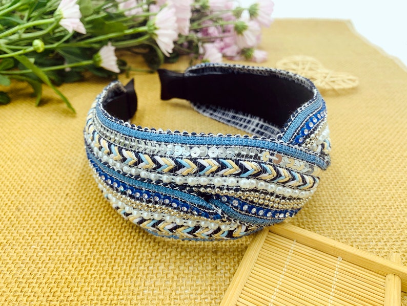 May include: A blue, white, and gold headband with a knotted design and beaded embellishments.