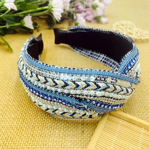 May include: A blue and white headband with a knotted design. The headband is decorated with sequins, beads, and a woven pattern.