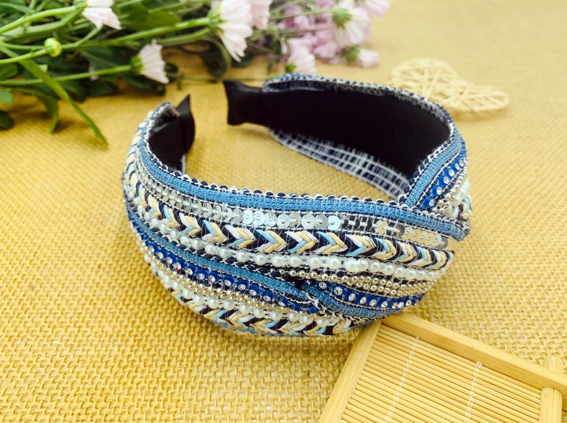 May include: A blue and white headband with a knotted design. The headband is decorated with sequins, beads, and a woven pattern.