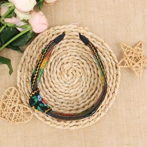 May include: A black headband with a colorful floral pattern. The headband is made of fabric and has a woven texture.