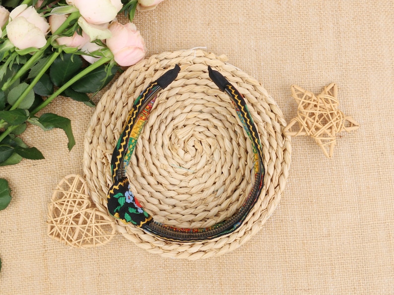 May include: A black headband with a colorful floral pattern. The headband is made of fabric and has a woven texture.
