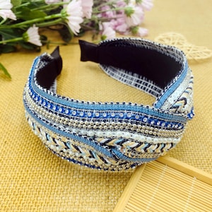 May include: A blue and white beaded headband with a knotted design. The headband is made of fabric and has a black elastic band.