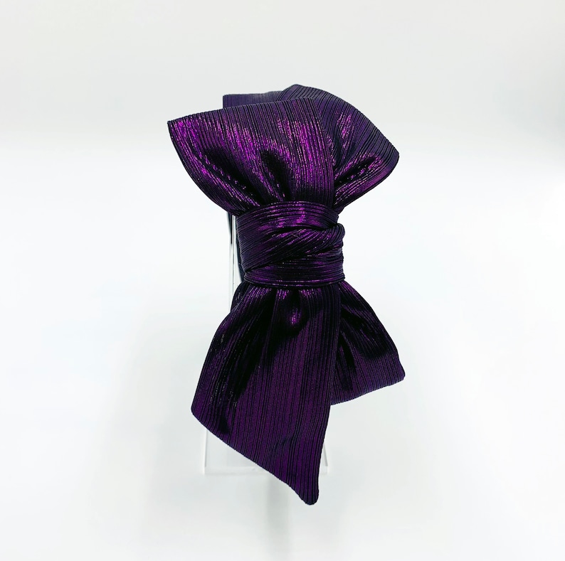 Pu&ograve; includere: Un cerchietto metallico viola con un grande fiocco. Il fiocco &egrave; annodato e le estremit&agrave; sono lasciate libere.