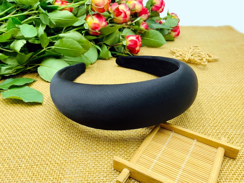 K&ouml;nnte beinhalten: Ein schwarzes gepolstertes Haarband. Das Haarband ist dick und breit und hat eine glatte, matte Oberfl&auml;che.