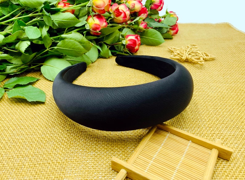 K&ouml;nnte beinhalten: Ein schwarzes gepolstertes Haarband. Das Haarband ist dick und breit und hat eine glatte, matte Oberfl&auml;che.