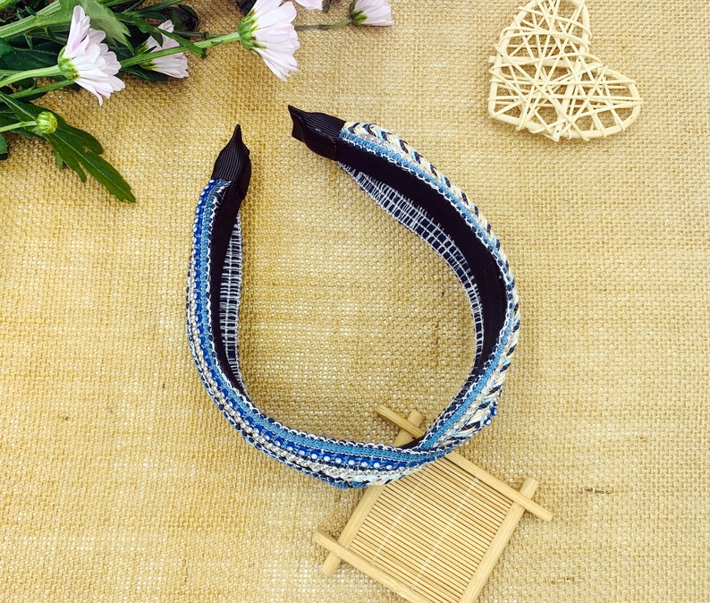 May include: A blue and white headband with rhinestones. The headband is made of a woven fabric and has a black elastic band.