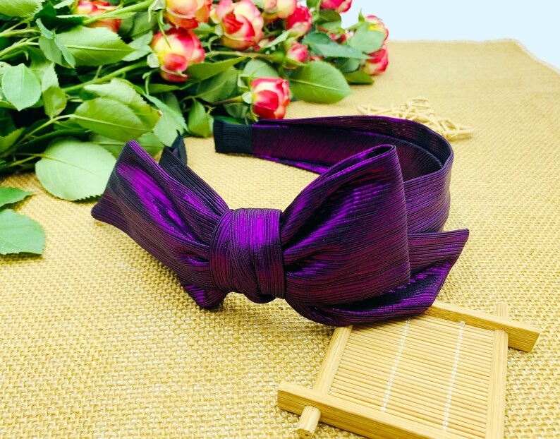 Pu&ograve; includere: Un cerchietto viola con un grande fiocco. Il cerchietto &egrave; realizzato in un tessuto lucido con un leggero luccichio.