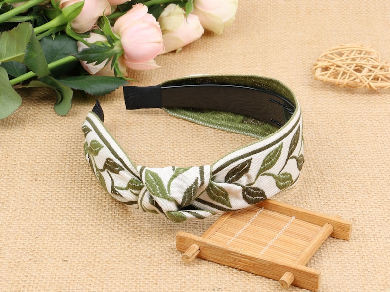 May include: A white headband with a green leaf pattern and a black elastic band. The headband is tied in a knot at the top.