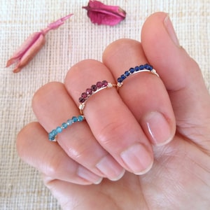 May include: Three delicate rings with a row of small gemstones. The rings are made of gold wire and feature blue, red, and teal gemstones.