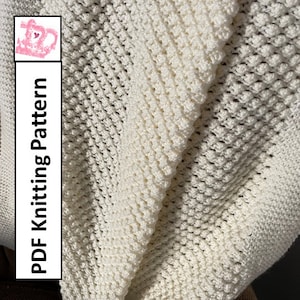 Op de afbeelding: Een wit gehaakt deken met een textuurpatroon. Het deken is dubbelgevouwen en de randen zijn zichtbaar. De tekst "PDF Knitting Pattern" staat verticaal aan de linkerkant van de afbeelding.