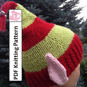 May include: A red and green striped knitted elf hat with pink elf ears. The hat has a bell and tassel on top. PDF Knitting Pattern.