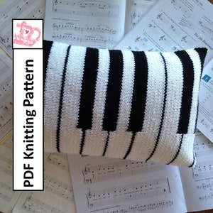 May include: A white and black knitted pillow shaped like a piano keyboard. The pillow is lying on top of sheet music.