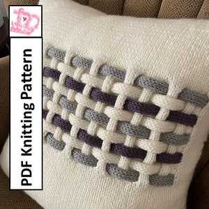 Könnte beinhalten: Ein weißes gestricktes Kissen mit einem gewebten Muster in Grautönen und Lila. Das Kissen liegt auf einem braunen Sessel. Der Text "PDF Knitting Pattern" ist vertikal auf der linken Seite des Bildes geschrieben.
