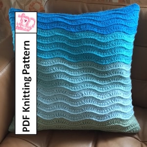 May include: A blue, green, and white knitted pillow with a wavy pattern. The pillow is on a brown leather couch. The text "PDF Knitting Pattern" is on the left side of the image.