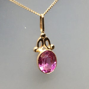 May include: A gold chain necklace with a pink oval gemstone pendant. The pendant has a delicate, ornate design.