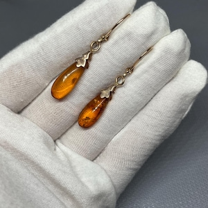 May include: A pair of gold teardrop earrings with amber stones. The earrings have a simple design and are perfect for everyday wear.